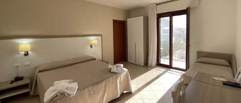 Quarto de hotel com duas camas, uma escrivaninha, um guarda-roupa e varanda com vista.