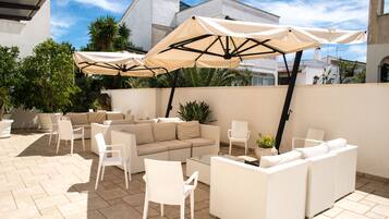 An outdoor patio with beige sofas, white chairs, and large umbrellas providing shade.