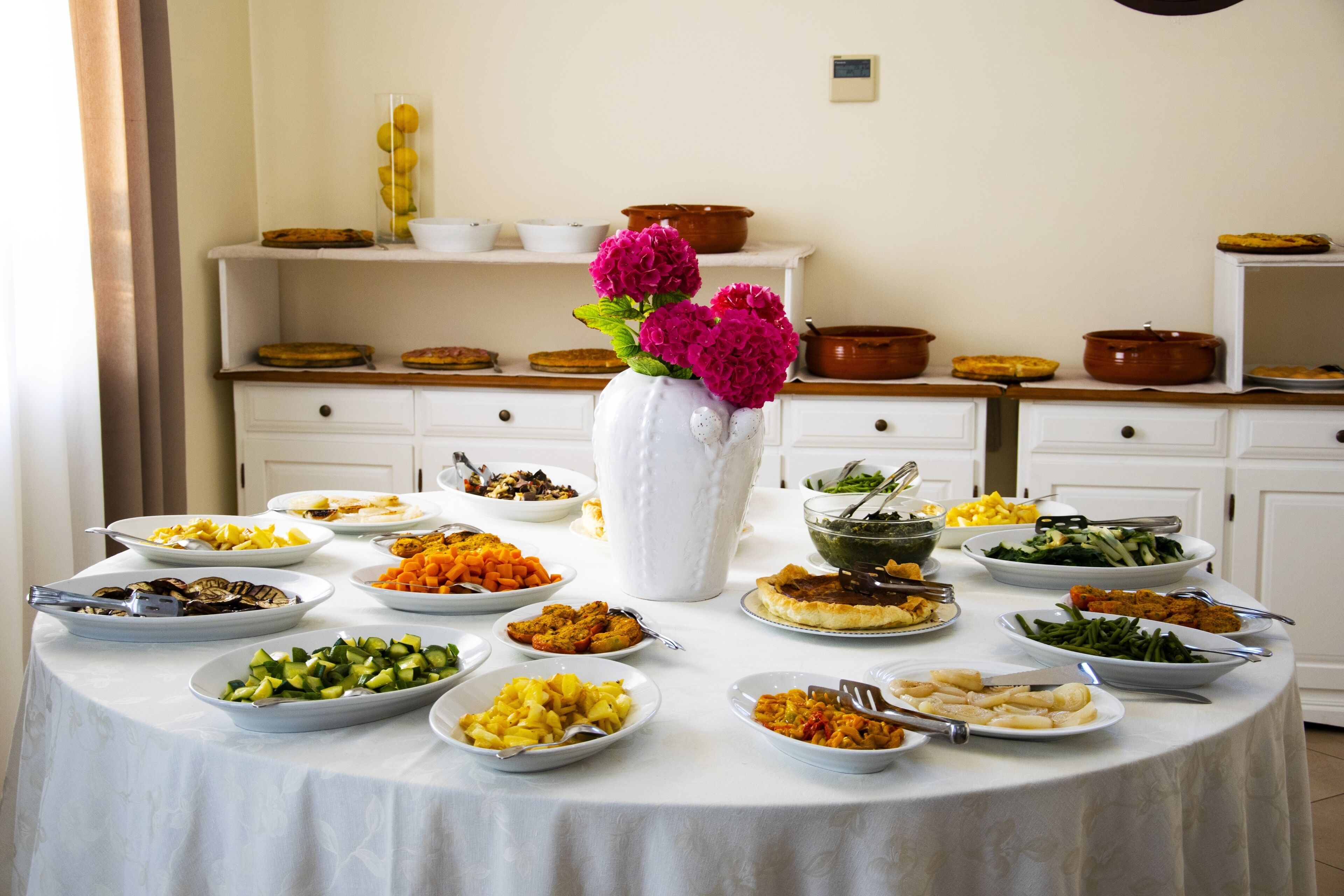 A buffet table with various dishes and a vase of flowers.