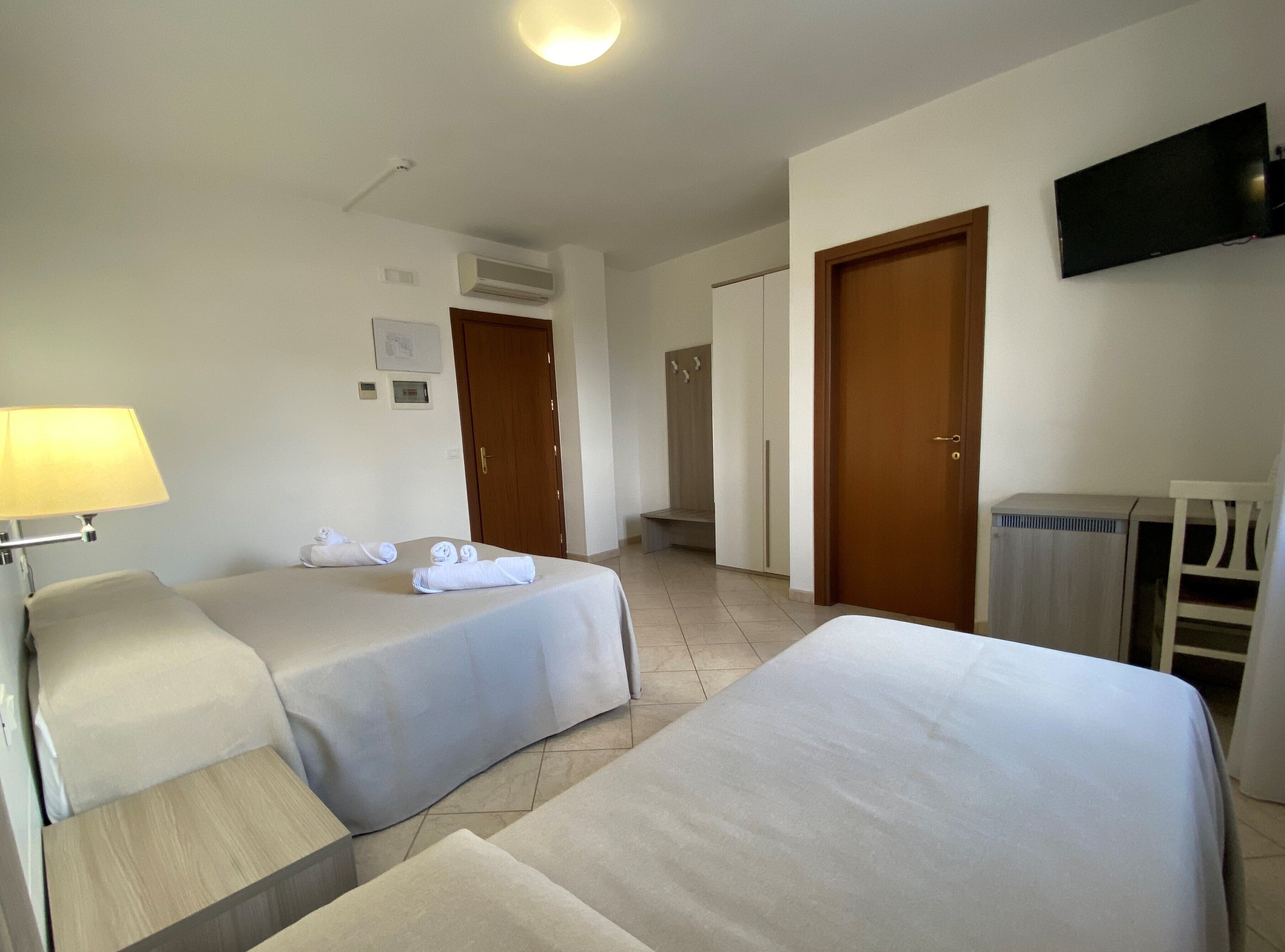 A hotel room with two beds, a TV, a lamp, and a desk.