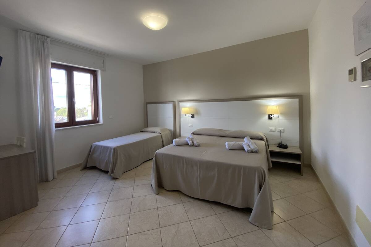 A hotel room with two beds, a window with curtains, a ceiling light, and a nightstand with a lamp.