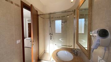 Une salle de bain avec une douche à parois de verre, un lavabo avec un miroir et un sèche-cheveux branché.