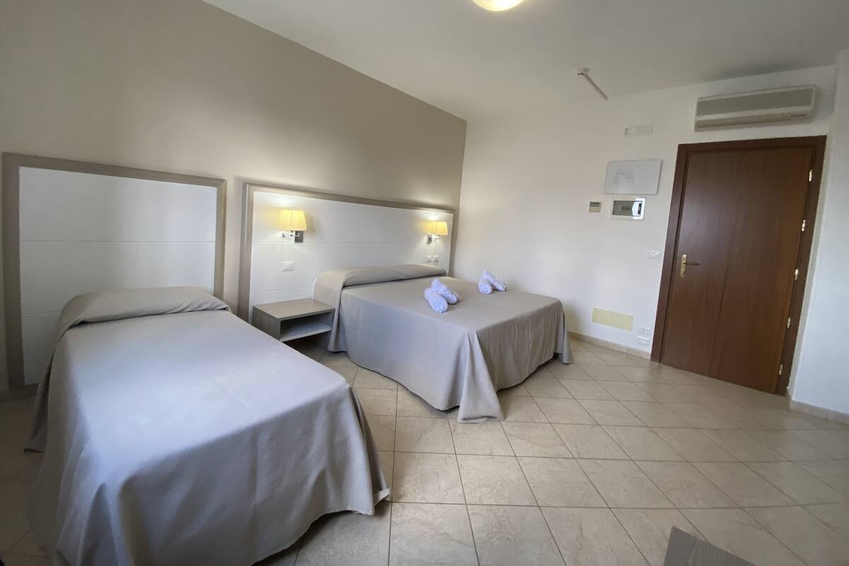 A hotel room with two beds, a nightstand, a lamp, and a door.