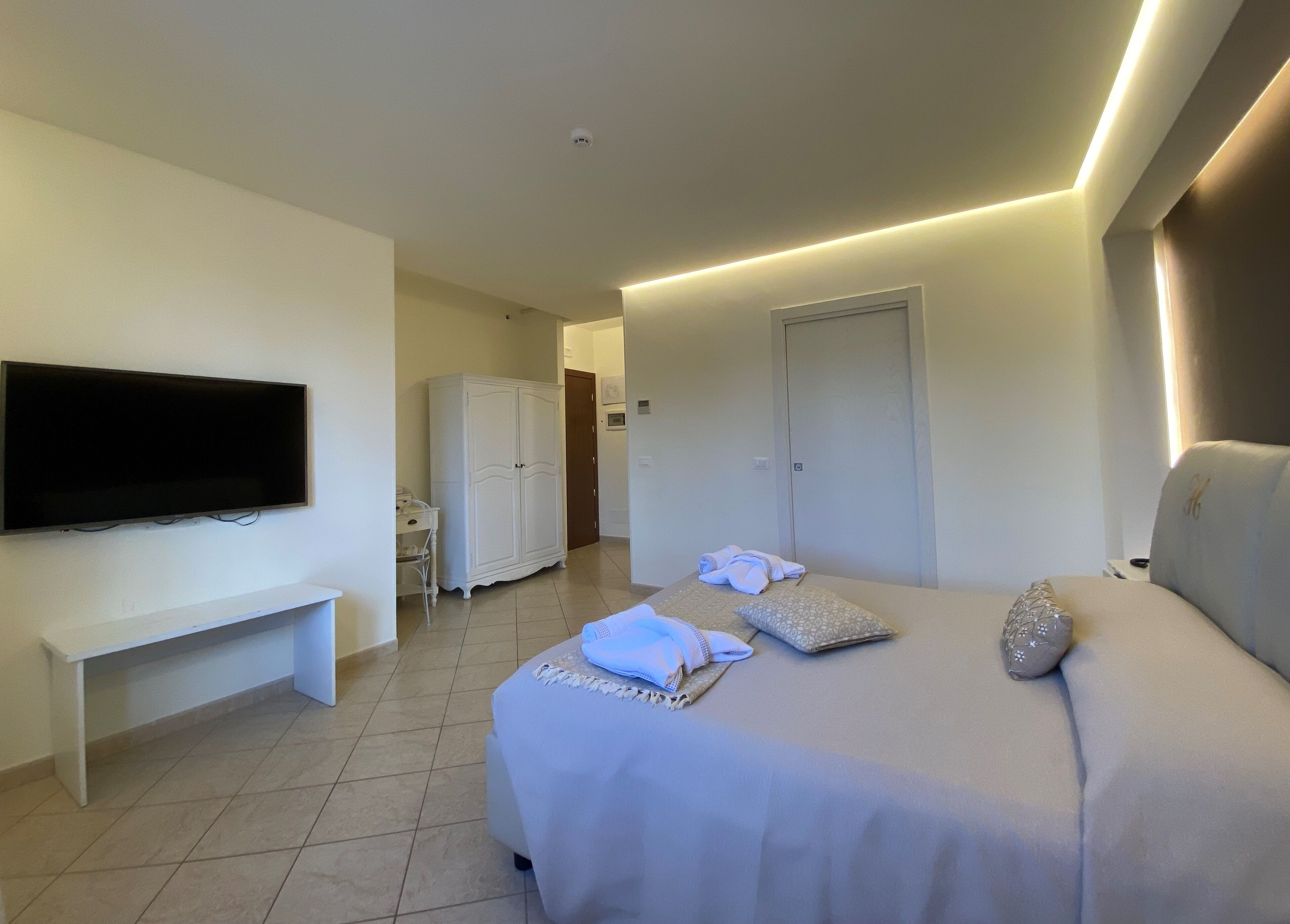 A hotel room with a bed, a TV mounted on the wall, a wardrobe, and a desk.