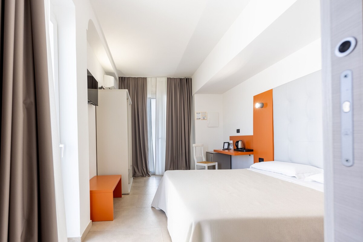 Habitación de hotel con cama, escritorio, silla y una pequeña mesa con cafetera.