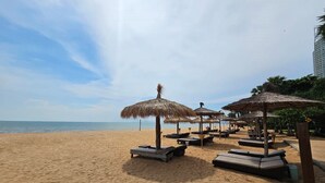 A beach with thatched umbrellas and lounge chairs, a clear sky, and a calm sea. - Botany Beach Resort Pattaya (Sattahip)