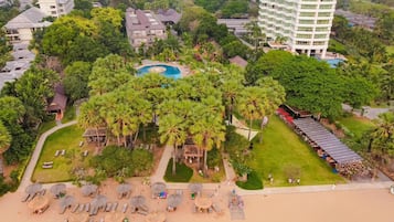 An aerial view of a resort with a swimming pool, palm trees, and a beach area with sun loungers and umbrellas.