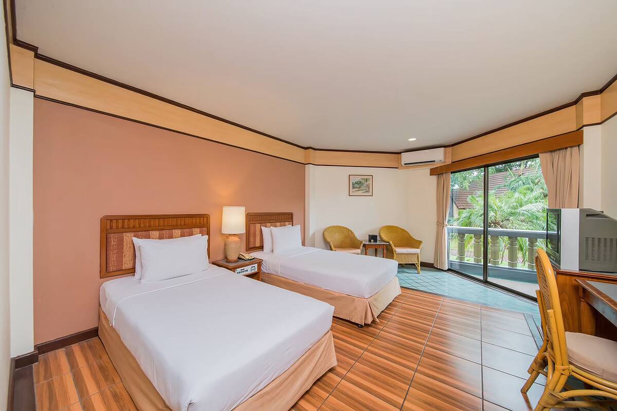Habitación de hotel con dos camas, un televisor, balcón con sillas y suelo de madera.