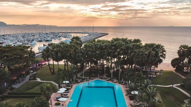 A large rectangular swimming pool with a circular island in the center, surrounded by palm trees and lounge chairs. - Botany Beach Resort Pattaya (Sattahip)