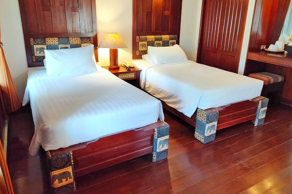Una habitación de hotel con dos camas, cabeceros de madera, una mesita de noche con lámpara y un armario de madera.