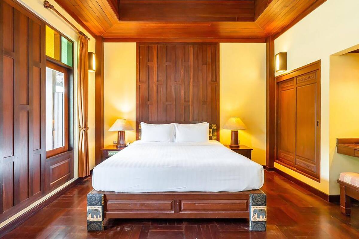 Una cama grande de madera con ropa blanca en una habitación con piso y paredes de madera.