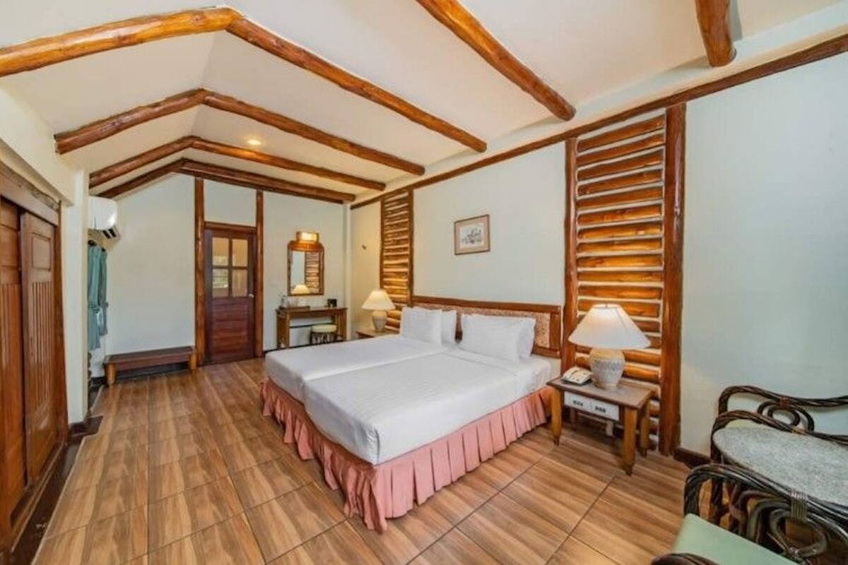 Un dormitorio con una cama grande, vigas de madera en el techo, un armario de madera y una mesita de noche con una lámpara.