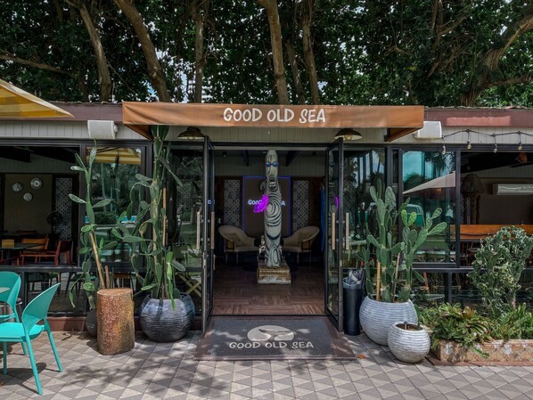 The entrance to a restaurant named "Good Old Sea" with a glass door, potted plants, and a neon sign.