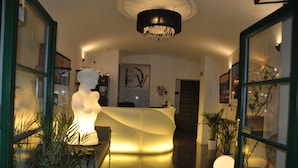 A hotel reception area with a modern design, featuring a curved reception desk, a chandelier, and potted plants.