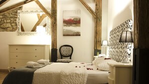 A bedroom with a wooden ceiling, a bed, a nightstand, a chair, and a wall-mounted lamp.