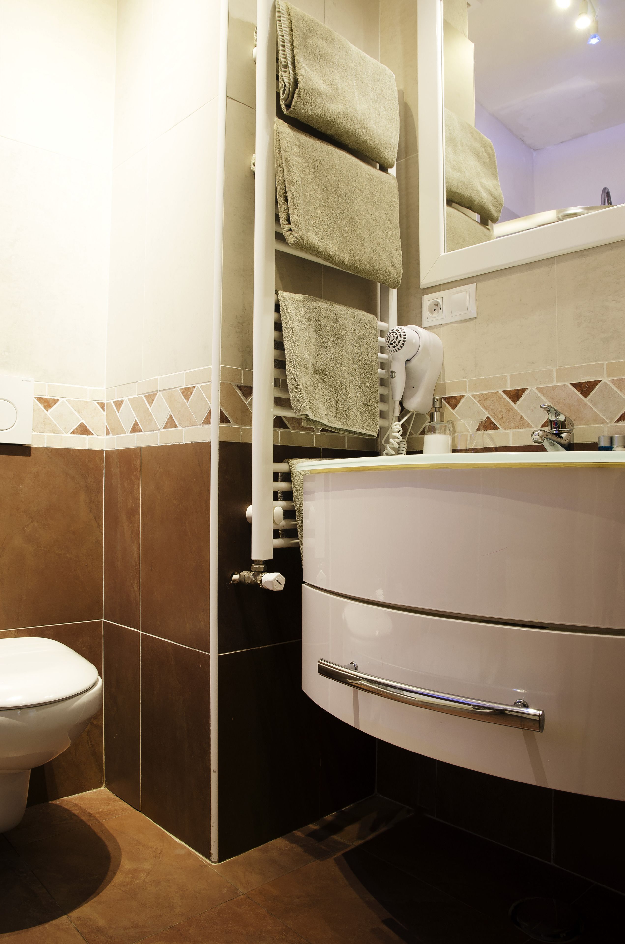 A bathroom with a white sink, a towel rack with folded towels, a hairdryer, and a toilet.