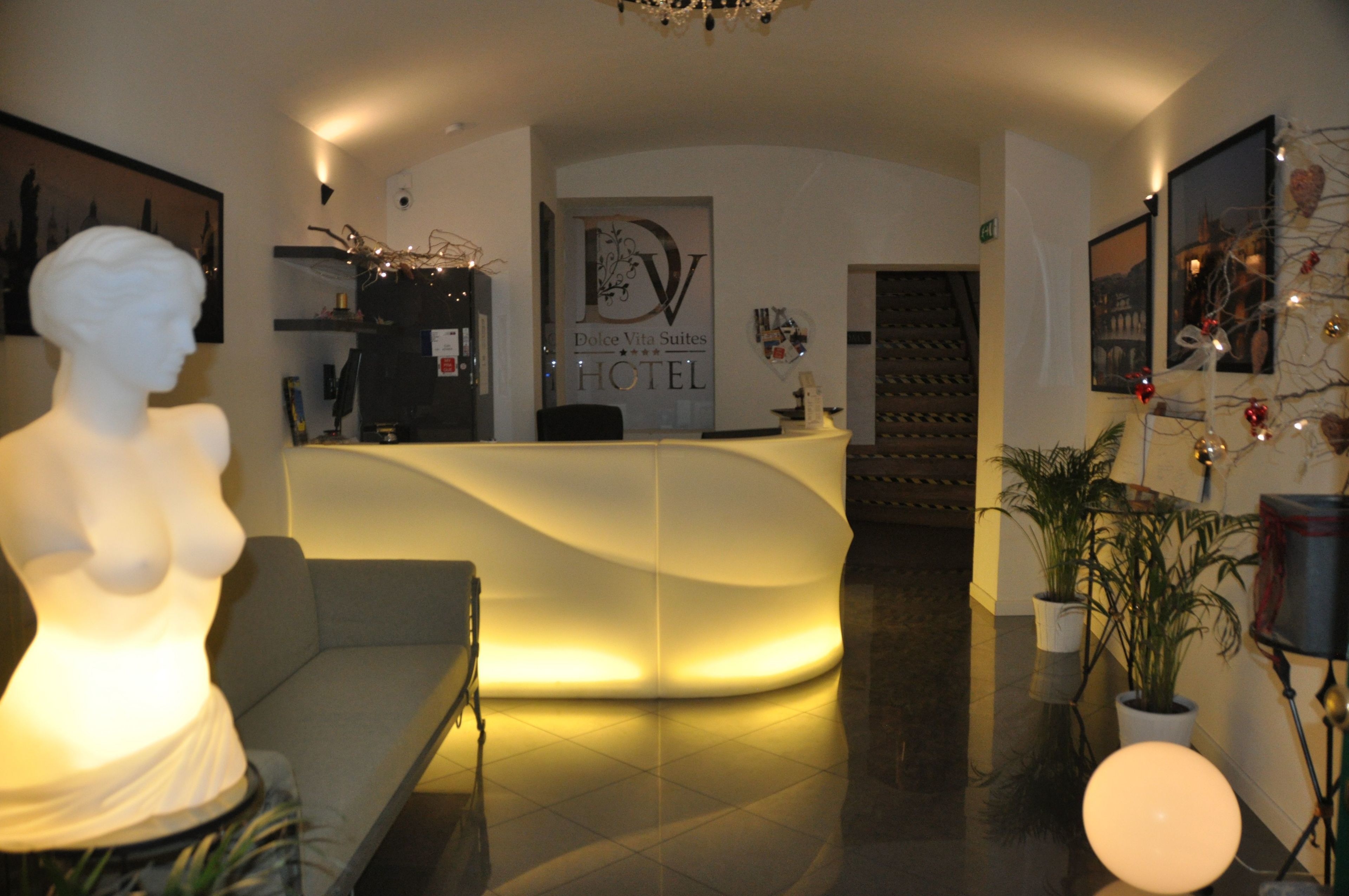 A hotel reception area with a modern design, including a reception desk, a sculpture, and potted plants.