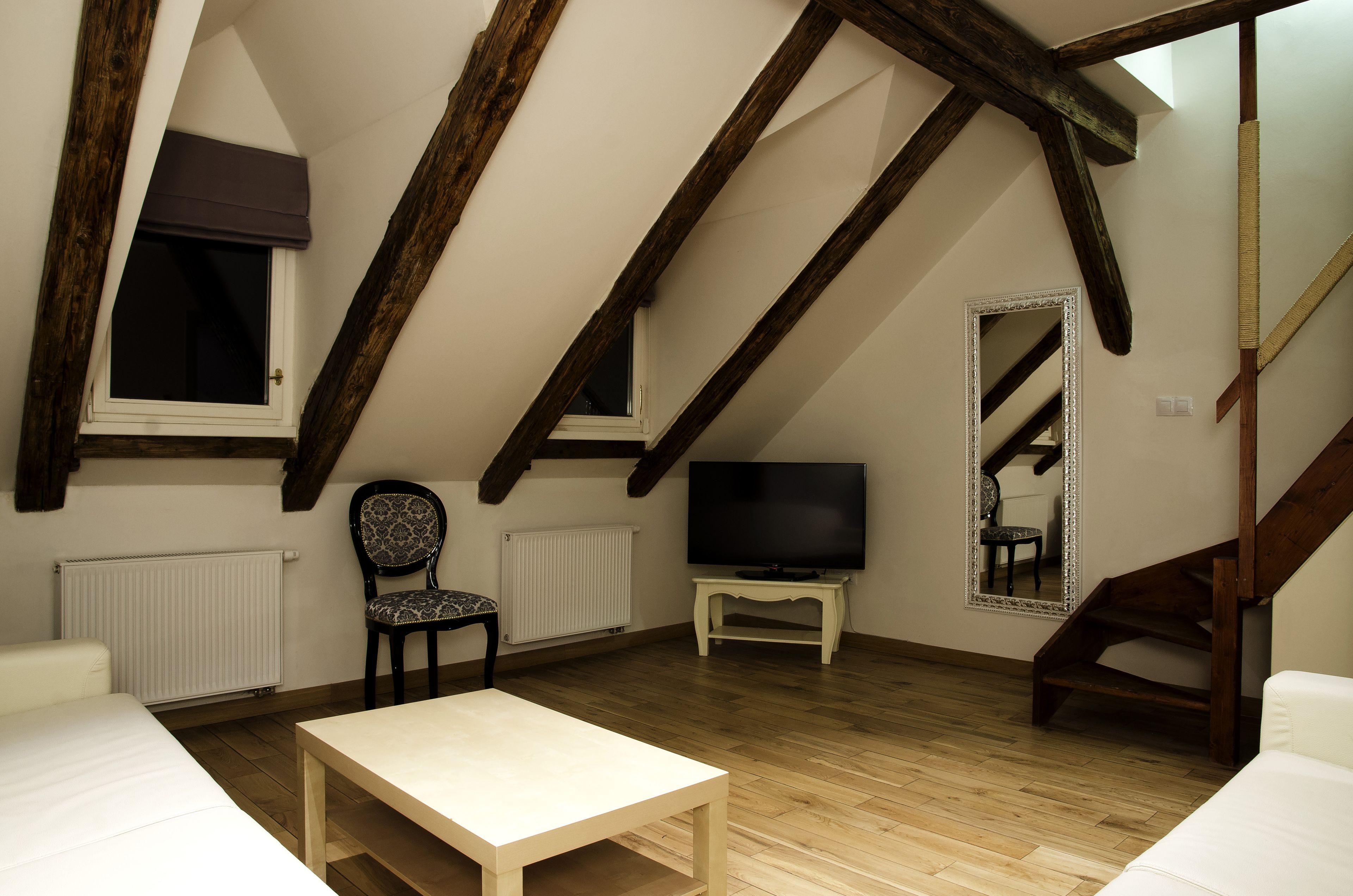 Dormitorio tipo loft con vigas de madera a la vista, una cama, un televisor, una silla y una mesita.