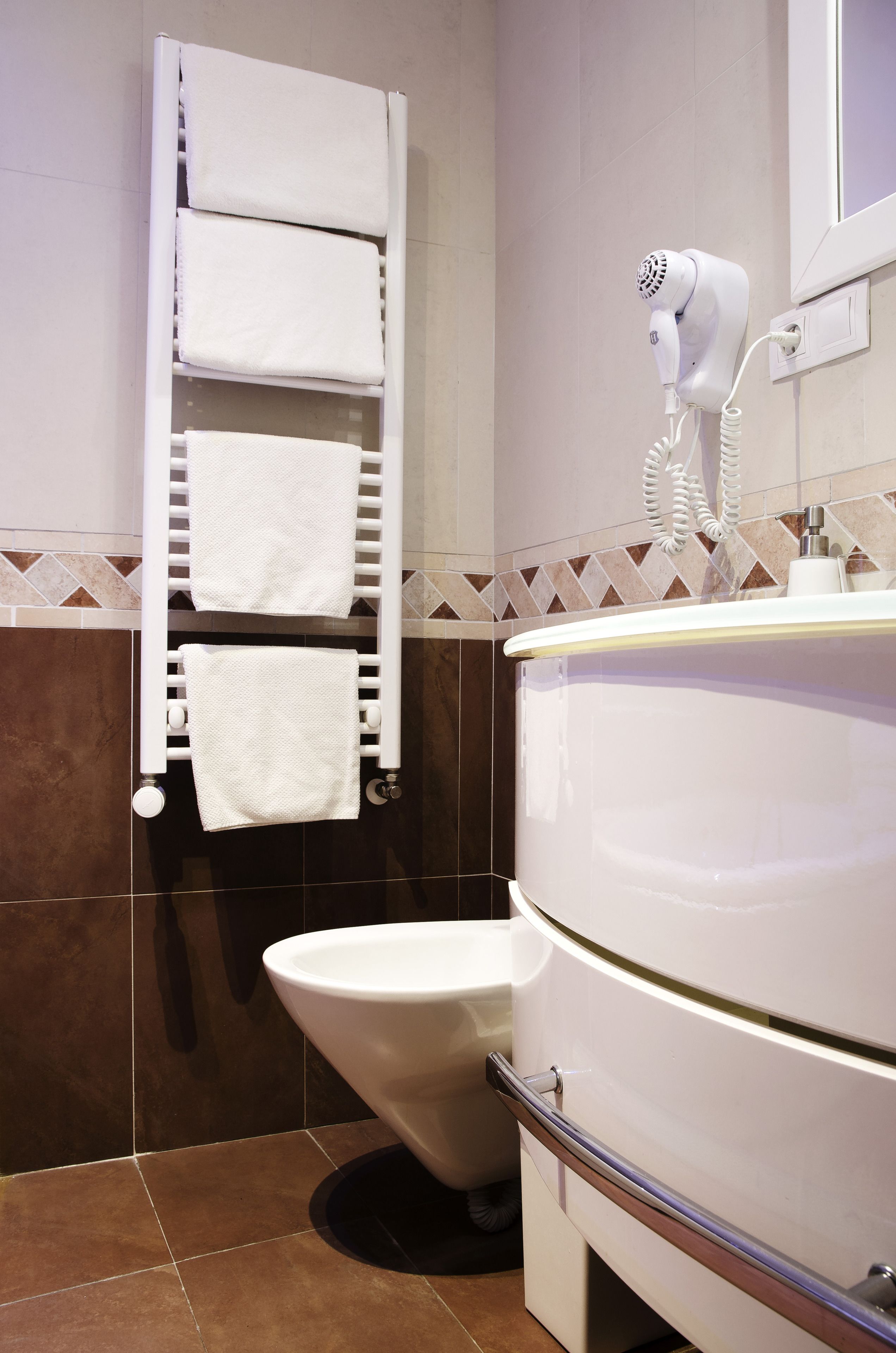 A bathroom with a white sink, a towel rack with folded towels, a hairdryer, and a toilet.