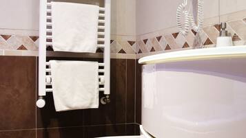 A bathroom with a white sink, a towel rack with folded towels, a hairdryer, and a toilet.