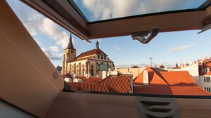 A view from a window overlooking a church with a tall spire and a red-tiled roof.
