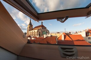 A view from a window overlooking a church with a tall spire and a red-tiled roof.