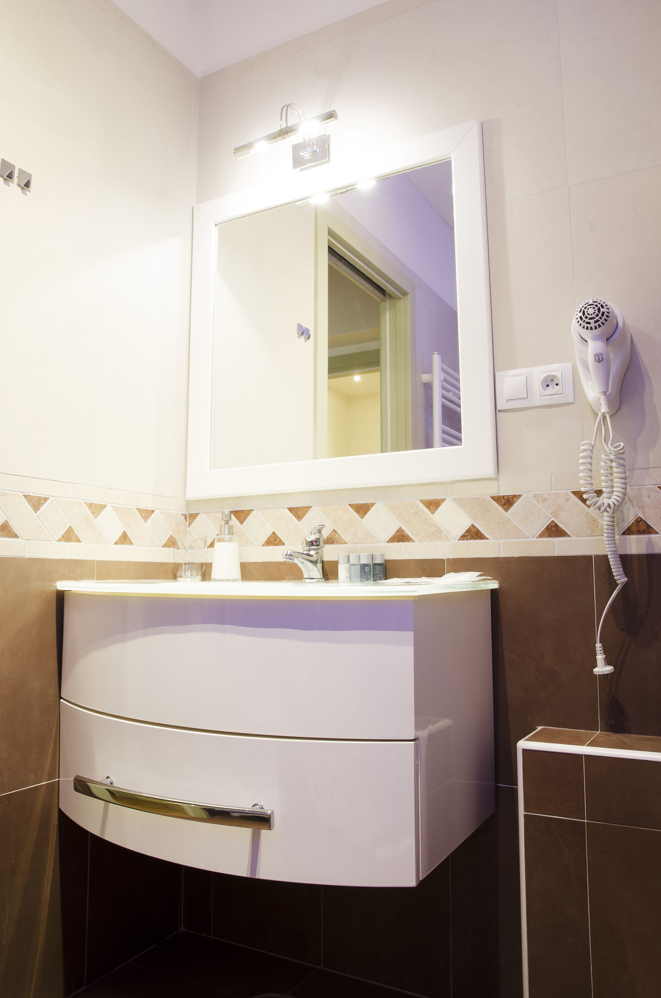 Et badeværelse med et hvidt toiletbord, et spejl, en hårtørrer og en håndklædestang.