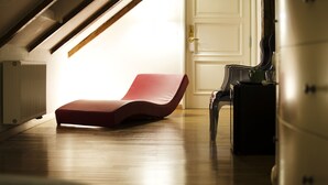 A sunlit room with a red lounge chair, a wooden floor, and a white door.