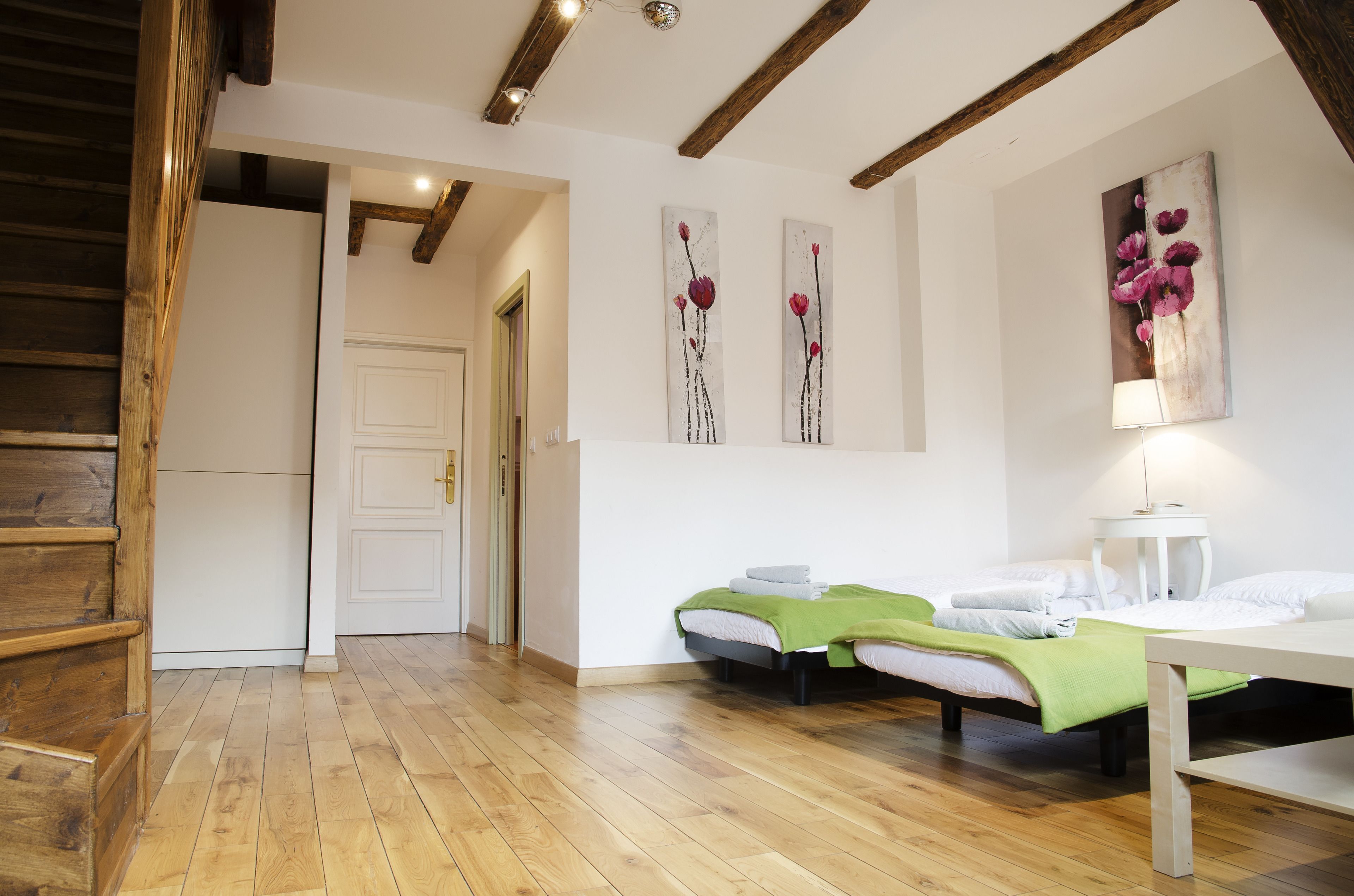 A room with two beds, wooden flooring, a staircase, and a door leading to another room.
