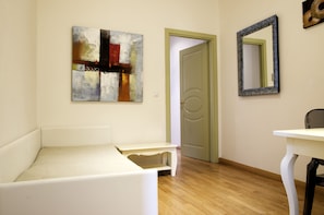 A room with a white sofa, a small table, a mirror, and an abstract painting on the wall.