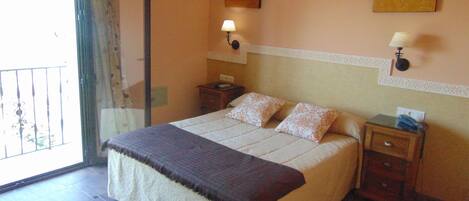 A hotel room with a bed, two bedside tables, a nightstand, a window with a view, and two wall-mounted lamps.