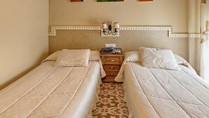 Een hotelkamer met twee eenpersoonsbedden, een nachtkastje met een lamp en drie aan de muur hangende bloemstillevens.
