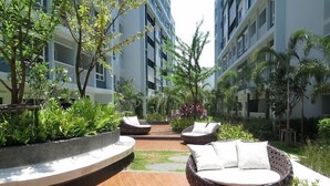 A courtyard with outdoor seating, surrounded by lush greenery and modern buildings. - The Trust Huahin Condo Garden View by Dome (Hua Hin)