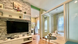A modern living room with a flat-screen TV, wooden flooring, a stone accent wall, a glass dining table, and a sofa. - The Trust Huahin Condo Garden View by Dome (Hua Hin)