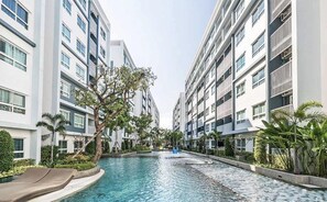 Un hotel moderno con piscina central, rodeado de exuberante vegetación y altos edificios.