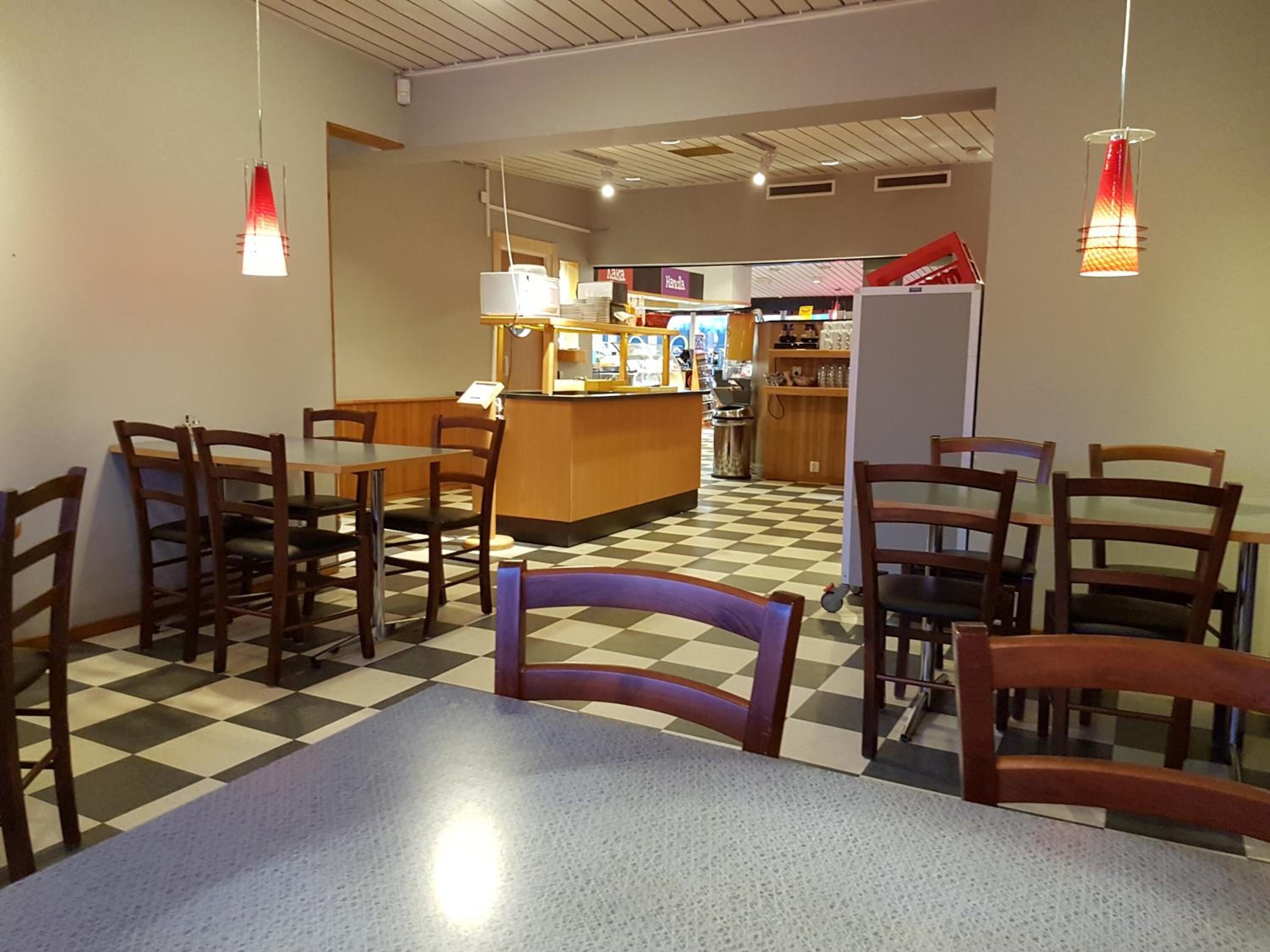 A restaurant with a checkered floor, wooden tables and chairs, a counter with a menu, and pendant lights.