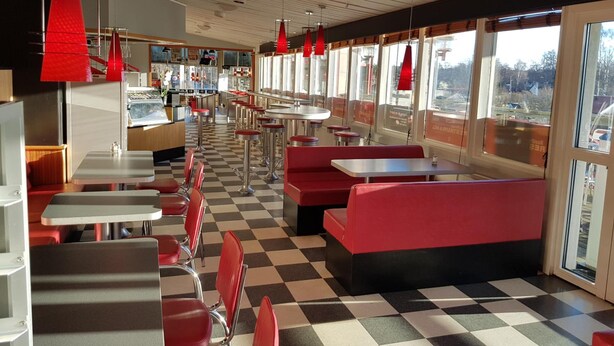 Un restaurant avec un sol à carreaux, des banquettes rouges et des tabourets de bar.