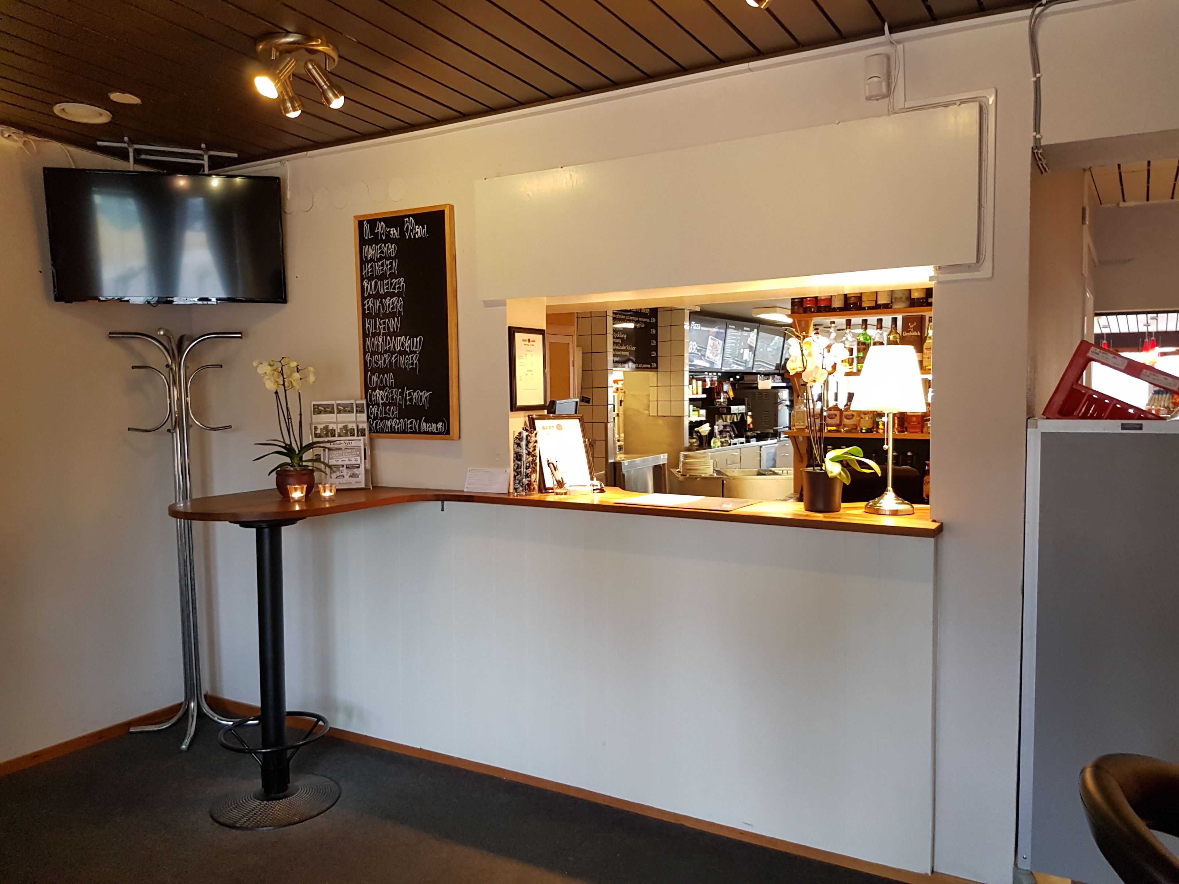 A reception area with a wooden counter, a television mounted on the wall, and a chalkboard menu listing various food items.