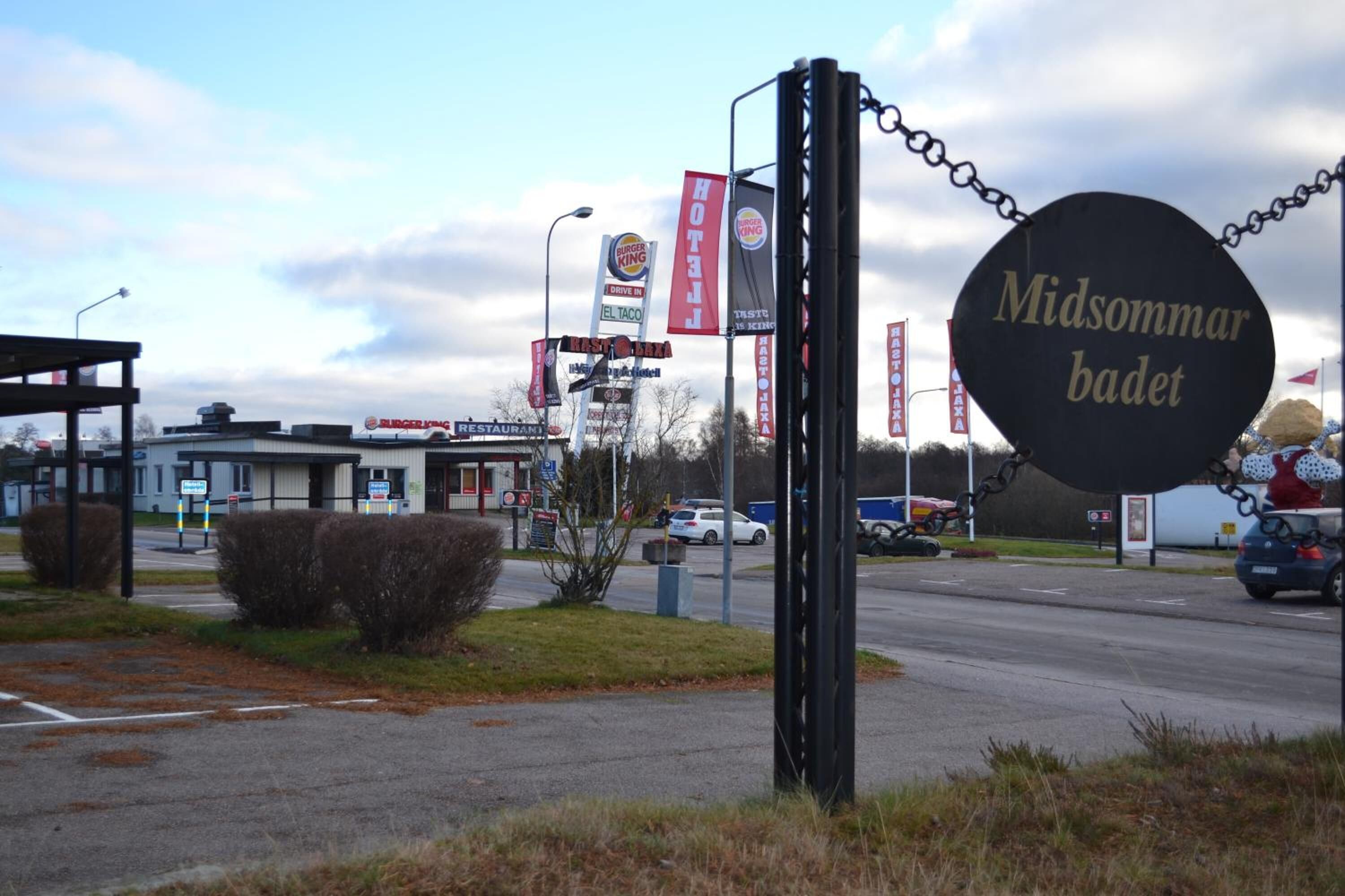 A sign for 'Midsommerbadet' with multiple banners for restaurants like Burger King and El Taco.