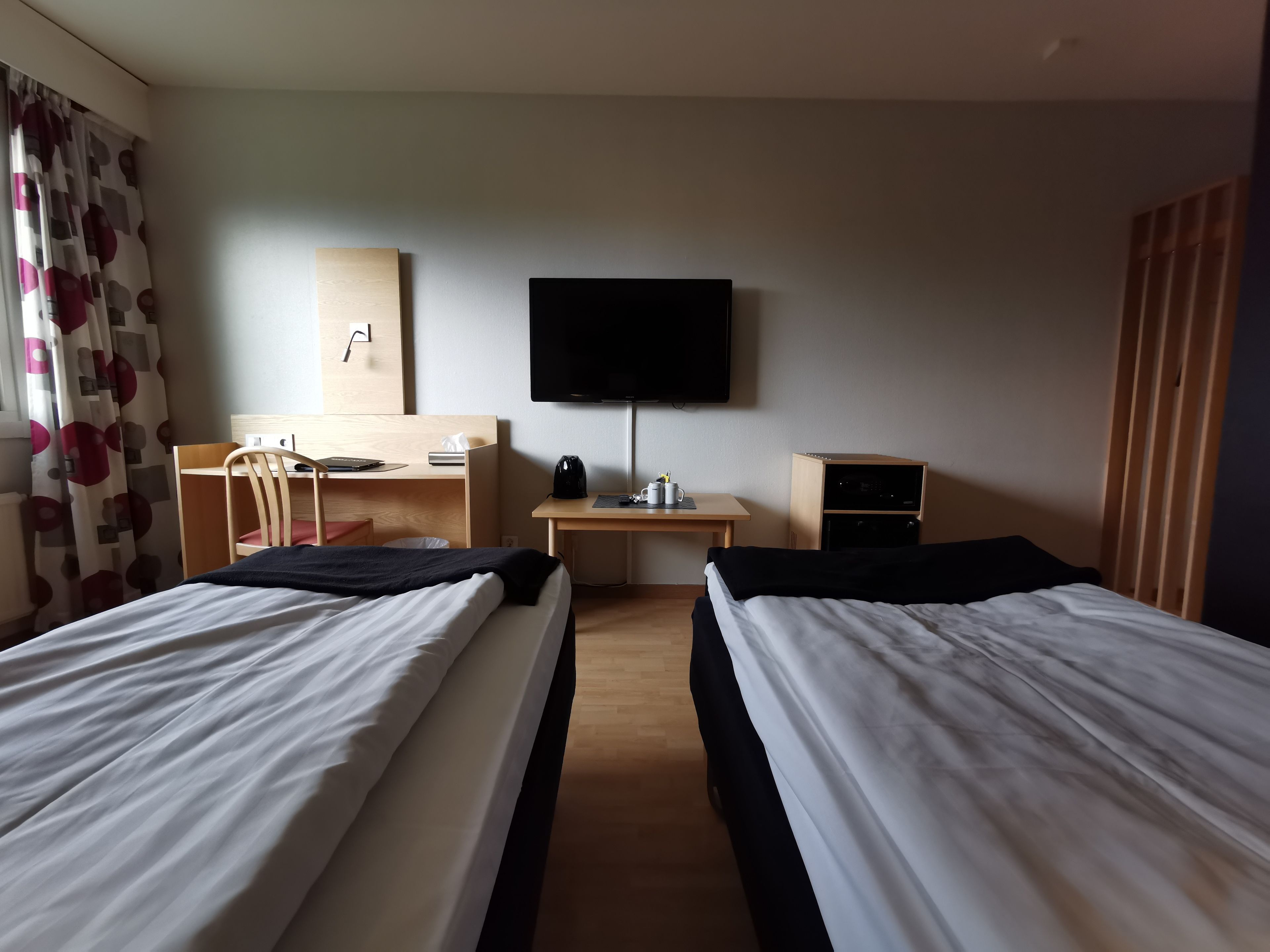 Een hotelkamer met twee bedden, een bureau, een stoel, een televisie en een klein kastje.