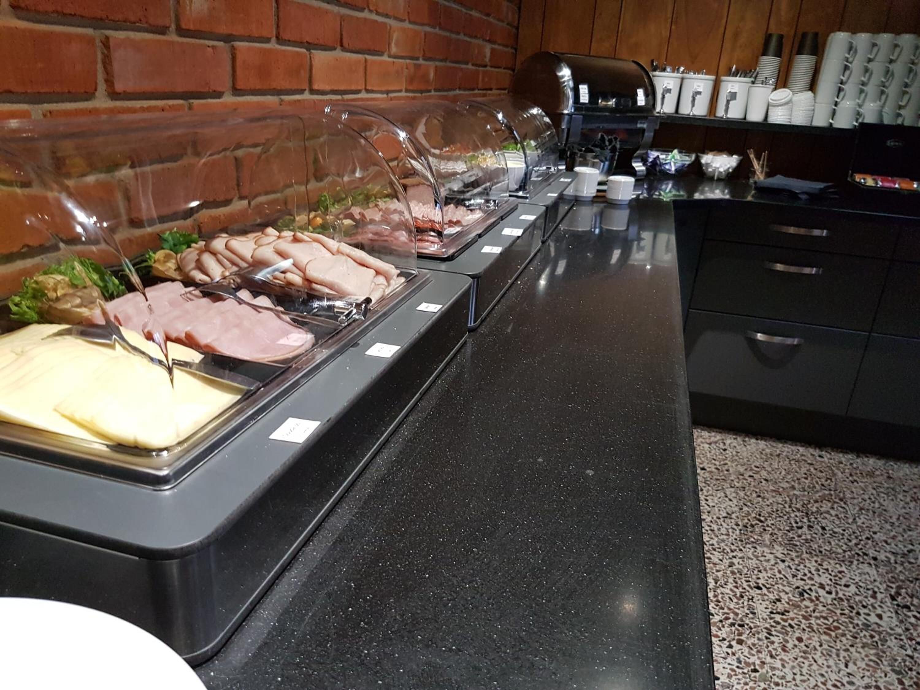 Een buffet met diverse gerechten, een koffieapparaat en een bakstenen muur op de achtergrond.