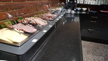 Un bufé con diferentes opciones de comida, una máquina de café y una pared de ladrillo al fondo.