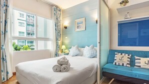 A hotel room with a bed, a blue sofa, a window with curtains, a wall-mounted lamp, and a framed picture. - The Trust Huahin Condo Pool View by Dome (Hua Hin)