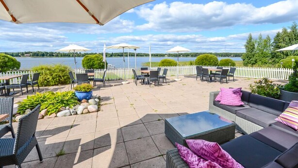 An outdoor patio with seating, umbrellas, and a view of a lake. - Hotel Sea Front (Raseborg)