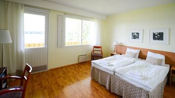 A room with a wooden floor, a bed with white bedding, a chair, a desk, and a window with curtains.