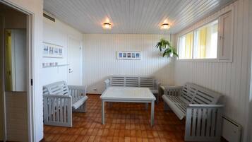A room with a tiled floor, white walls, a white bench, a table, and a hanging plant.