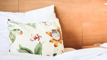 A hotel room with a wooden headboard, white bedding, and a floral-patterned pillow.