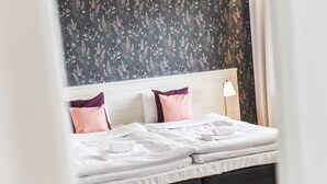A neatly made bed with white linens and two pillows, one pink and one purple, against a wall with a floral wallpaper pattern. - Hotel Sea Front (Raseborg)