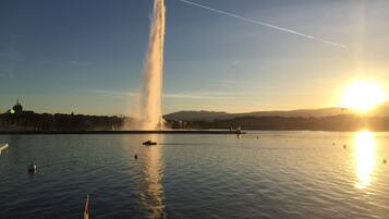 A boat on calm water with a fountain in the background and a sunset.