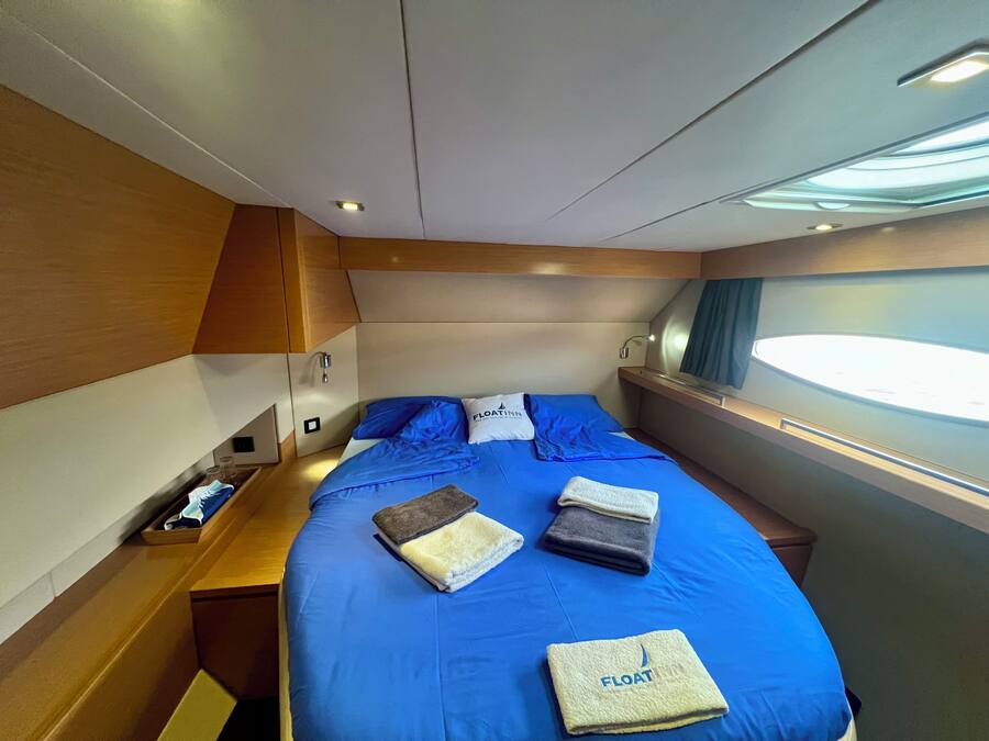 A compact, modern bedroom with a blue bedspread, neatly folded towels, and a window providing natural light.